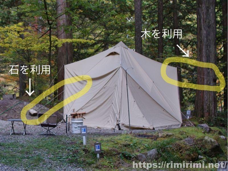 狭い林間サイトでスカイパイロットTCを設営するため、石と木の両方を利用してロープを固定している様子